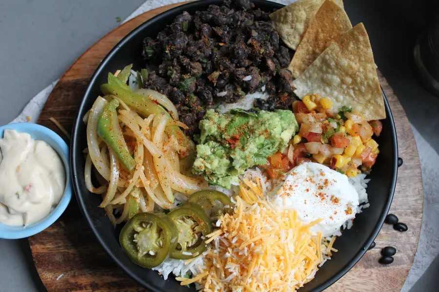 Colorful Mexican burrito bowl with guacamole, black beans, rice, corn, and cheese