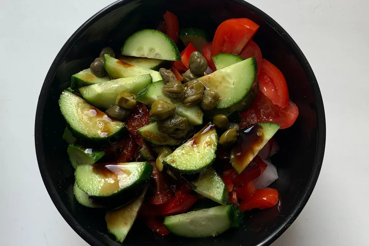 Top-down bowl of cucumber tomato salad with herbs and capers