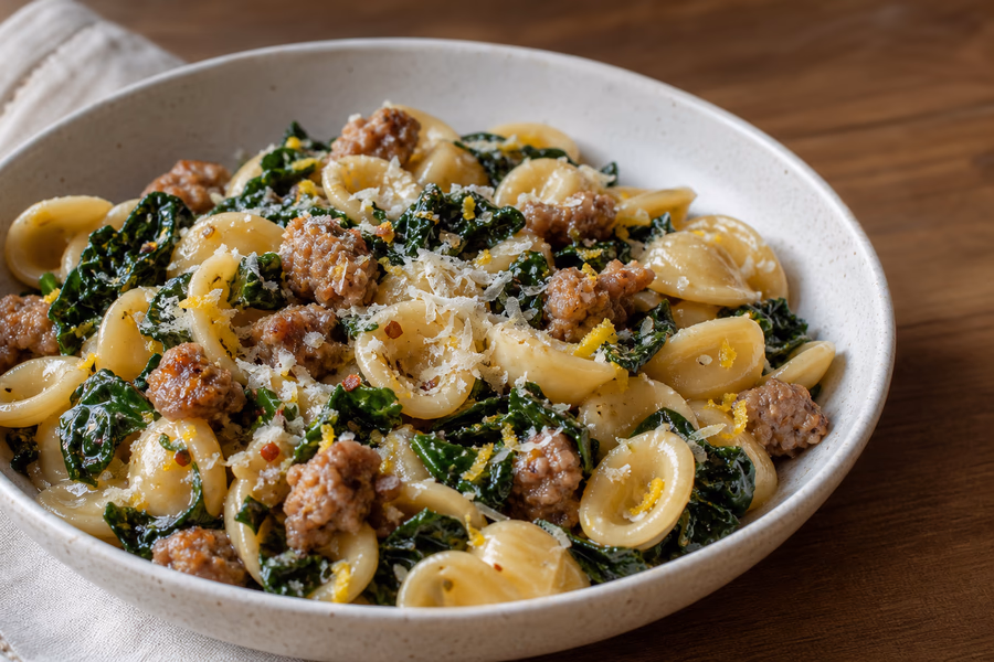 Bowl of short pasta with browned sausage, dark leafy greens, lemon zest, and parmesan